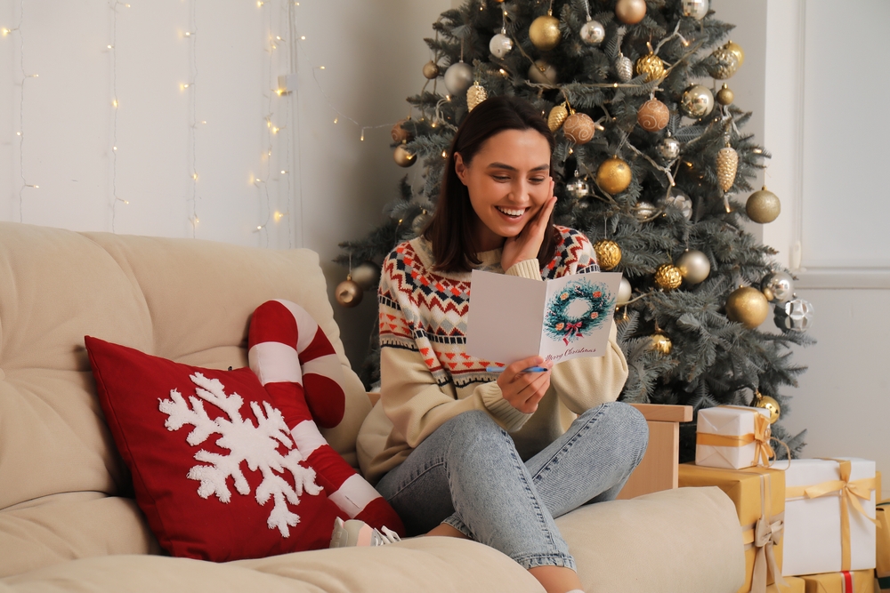 Happy,Young,Woman,Reading,Christmas,Greeting,Card,While,Sitting,On